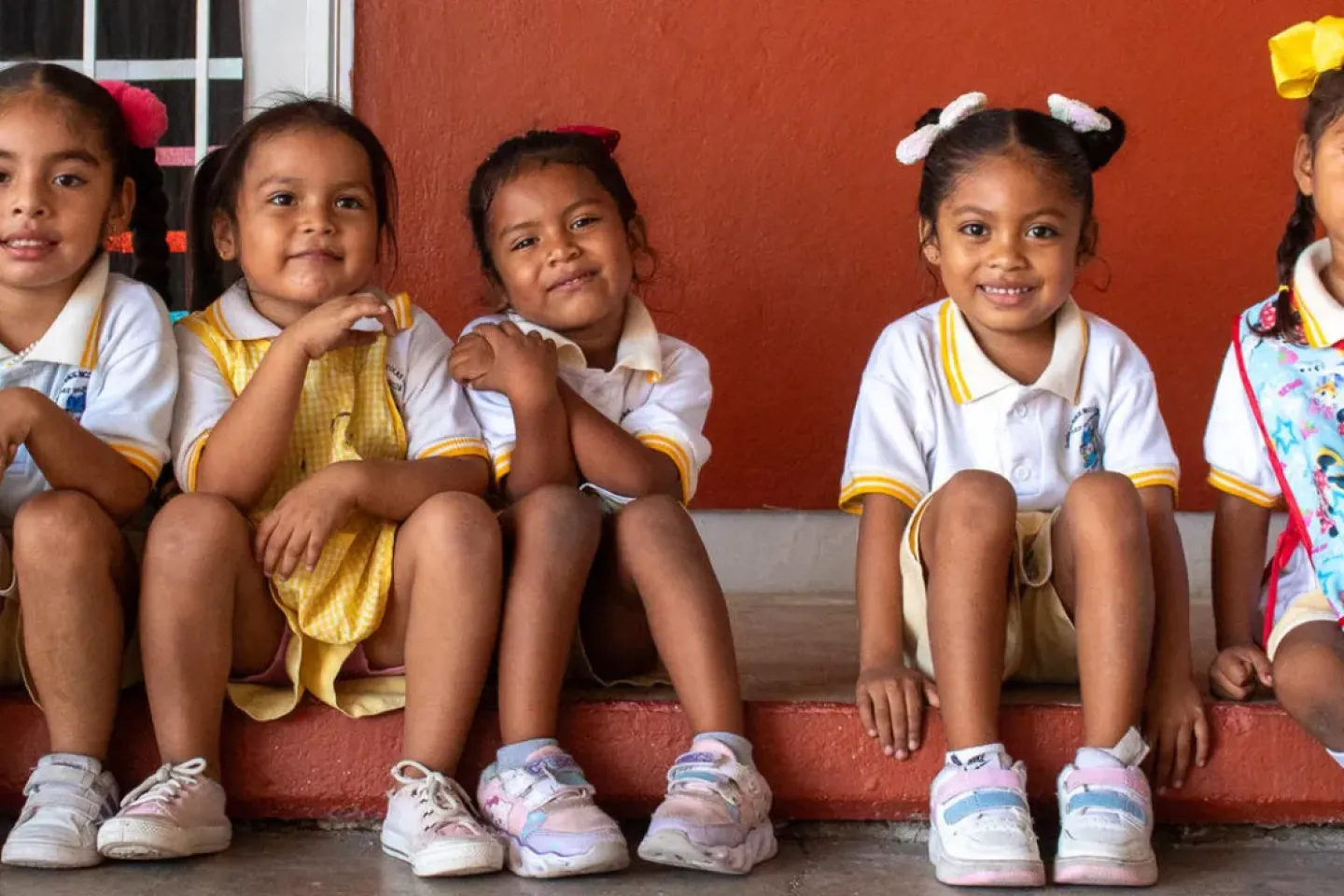 Cinco ni&ntilde;as con uniforme escolar sentadas en las escaleras de su escuela.