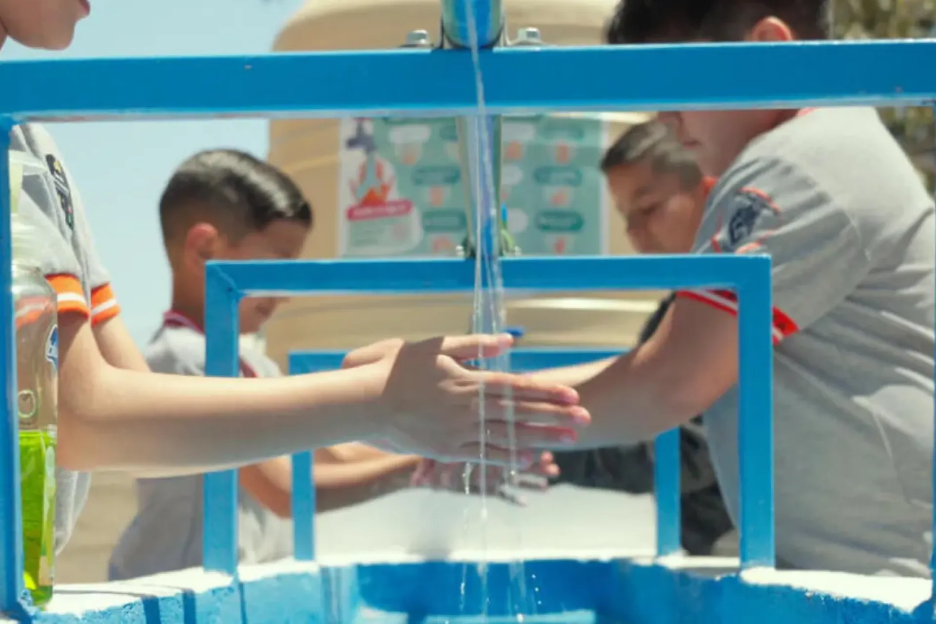 Ni&ntilde;os lavando sus manos en una toma de agua comunitaria de color azul al exterior de una escuela