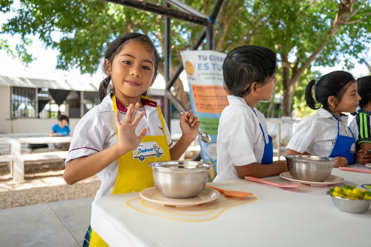 Ni&ntilde;a con delantal participa en una actividad de cocina saludable del Nutrim&oacute;vil junto a otras ni&ntilde;as y ni&ntilde;os.