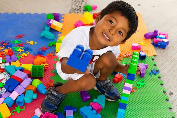 Un ni&ntilde;o sonr&iacute;e mientras juega con bloques de colores sobre un tapete de fomi en un espacio de juego.