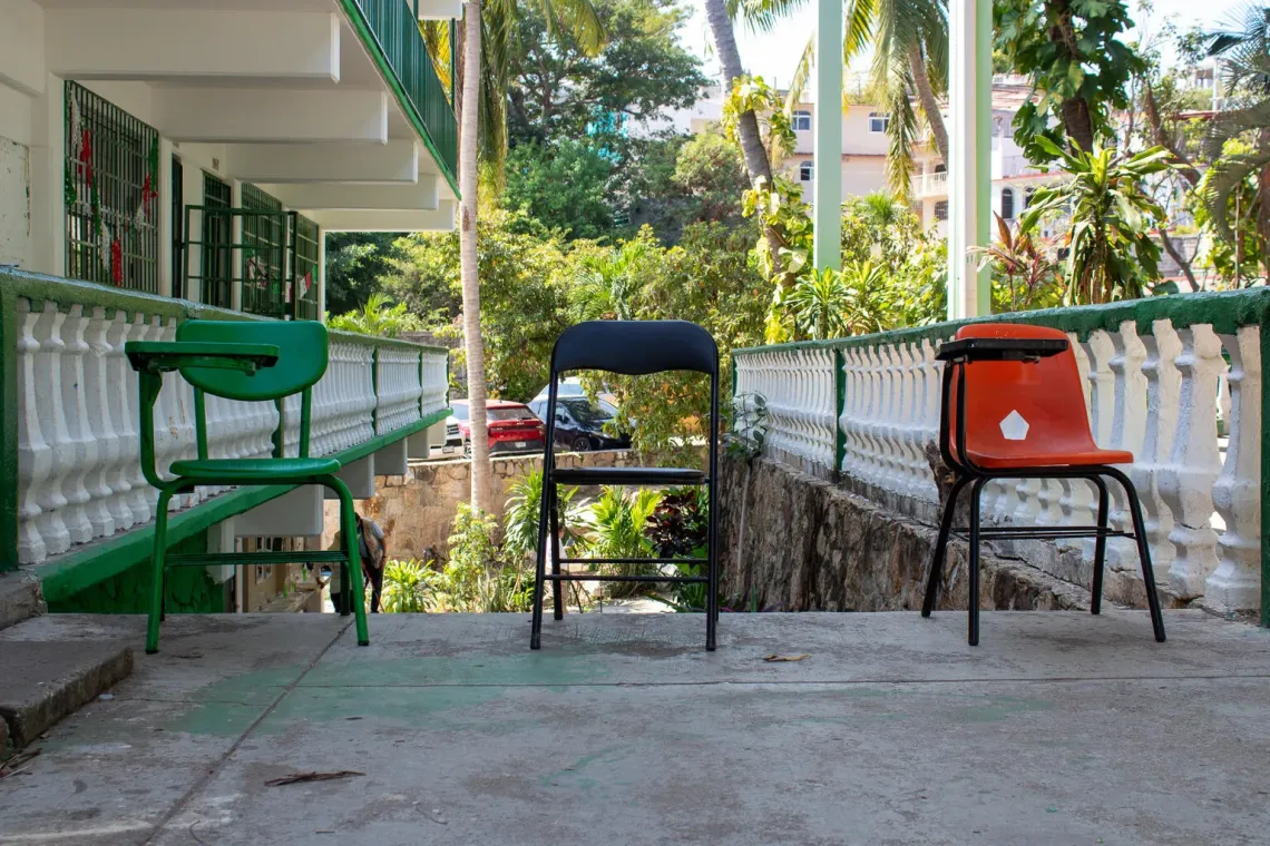 Tres pupitres vac&iacute;os est&aacute;n en el exterior de una escuela en medio de un proceso de rehabilitaci&oacute;n luego de afrontar una emergencia