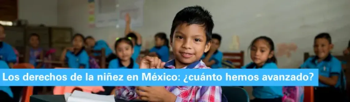 Un ni&ntilde;o est&aacute; en un sal&oacute;n de clases de su escuela mirando frente a la c&aacute;mara, detr&aacute;s de &eacute;l se encuentran varios de sus compa&ntilde;eros y compa&ntilde;eras de clase