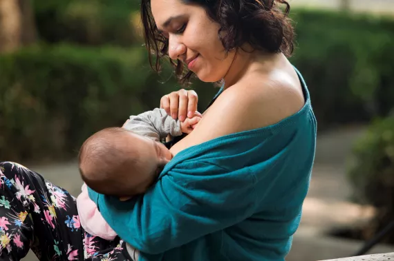 Una mam&aacute; sostiene a un beb&eacute; entre brazos mientras lo amamanta y lo cubre con un fular verde