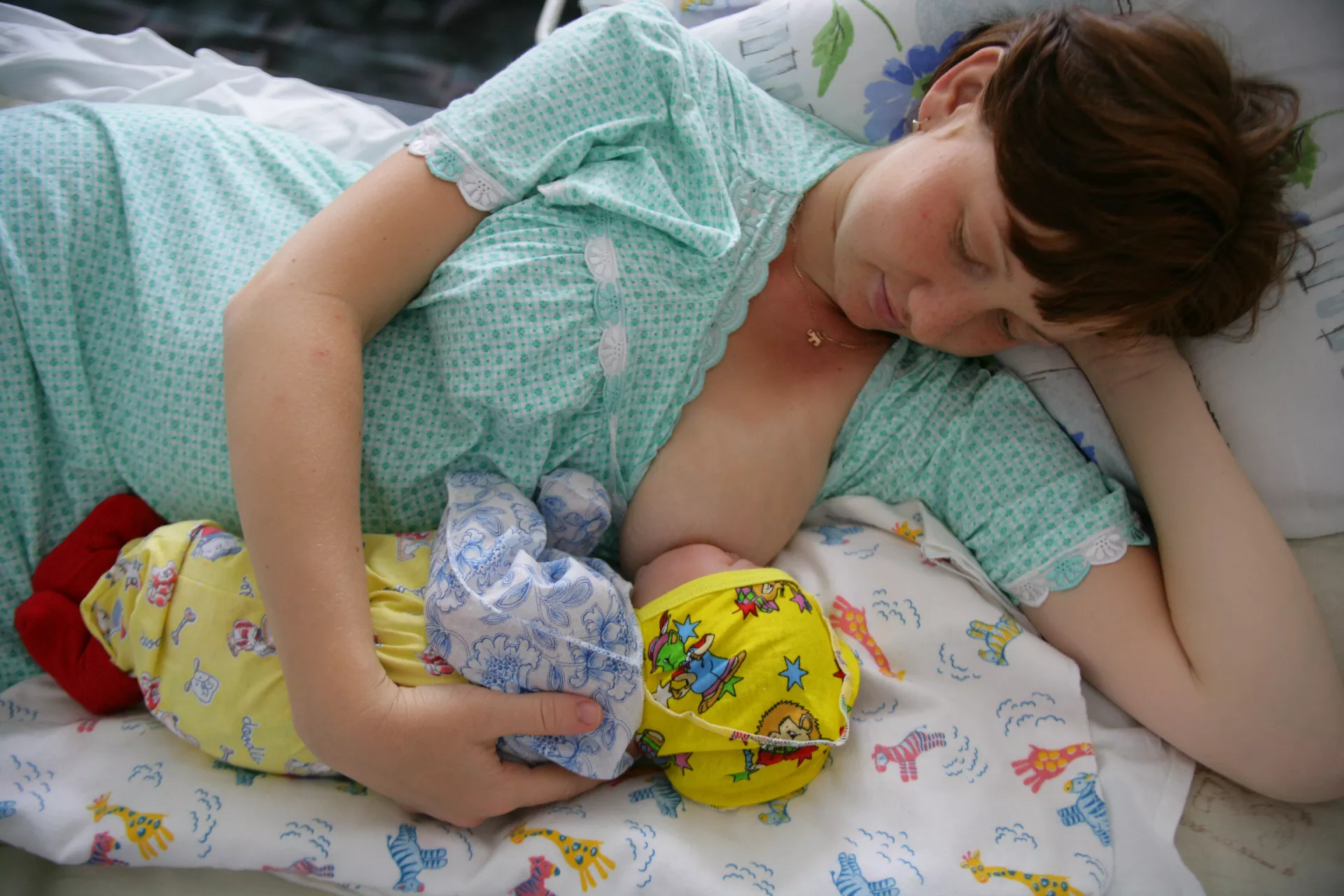 A mother lovingly looks down at her baby while breastfeeding as she lies on a bench. 