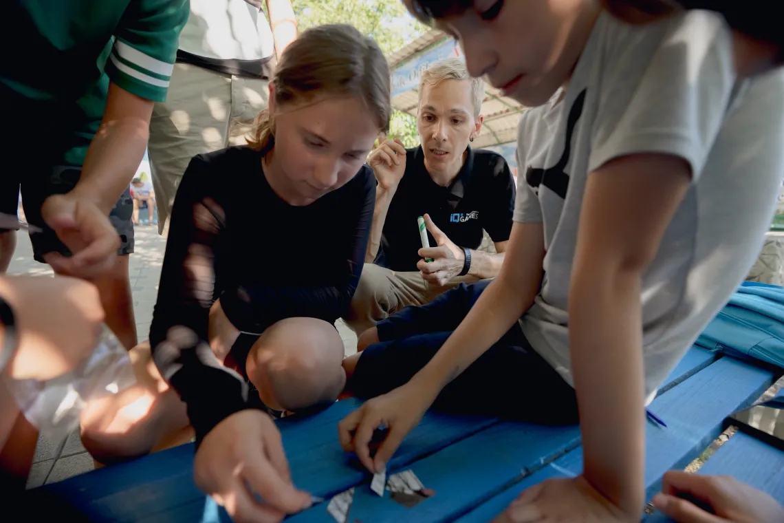 Un grup de copii de la tabăra de vară fac un puzzle &icirc;n timp ce sunt ghidați de unul dintre organizatorii jocului. 