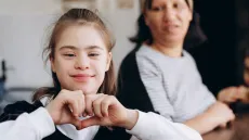 young girl with down syndrome creating a heart gesture with hands