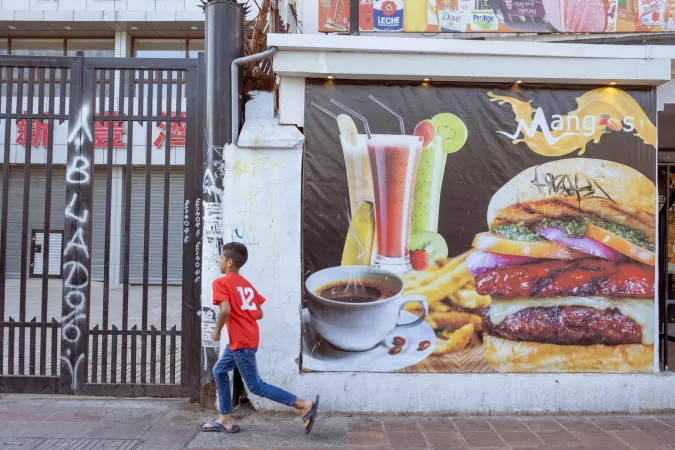 On 25 November 2022 in the city centre of Santiago, Chile, a child runs past a billboard for fast food on his way to a candy store. Colourful and eye-catching advertising such as this makes the food promoted more appealing to children and adolsecents.