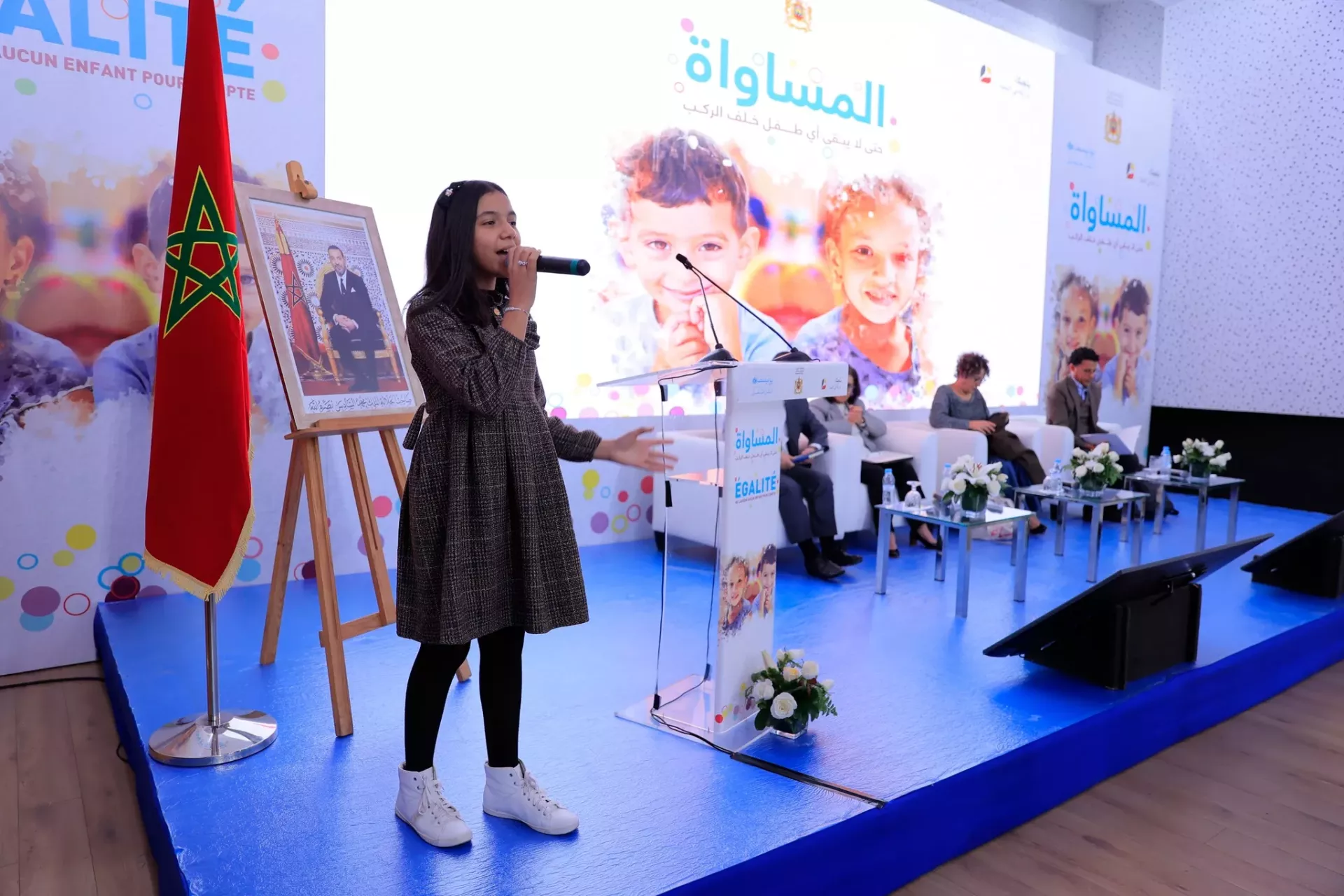 Une jeune fille marocaine, debout sur un podium, s'adresse &agrave; une audience en utilisant un microphone qu'elle tient dans la main.