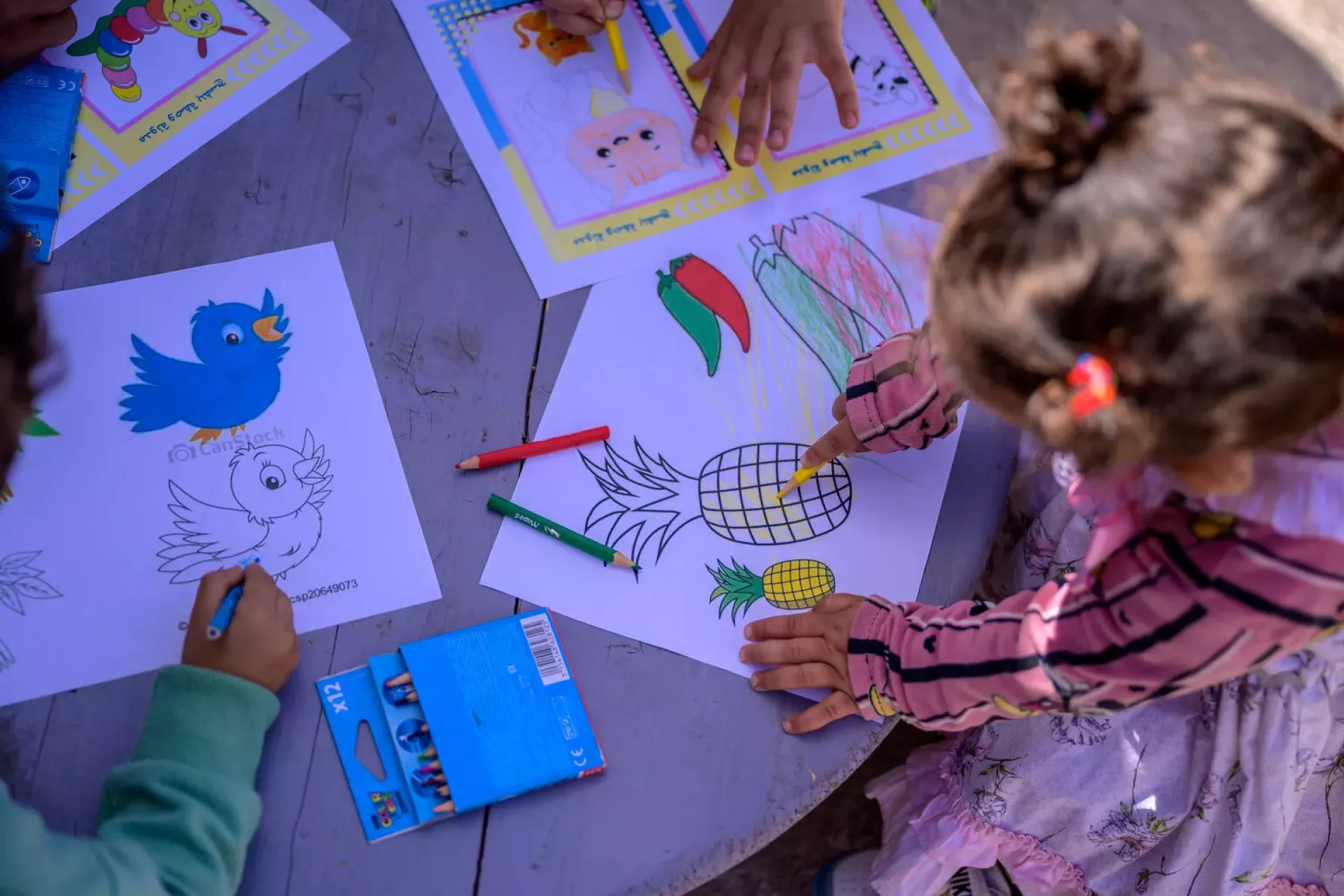 Des enfants font du coloriage sur une table en bois, utilisant des crayons de couleur.