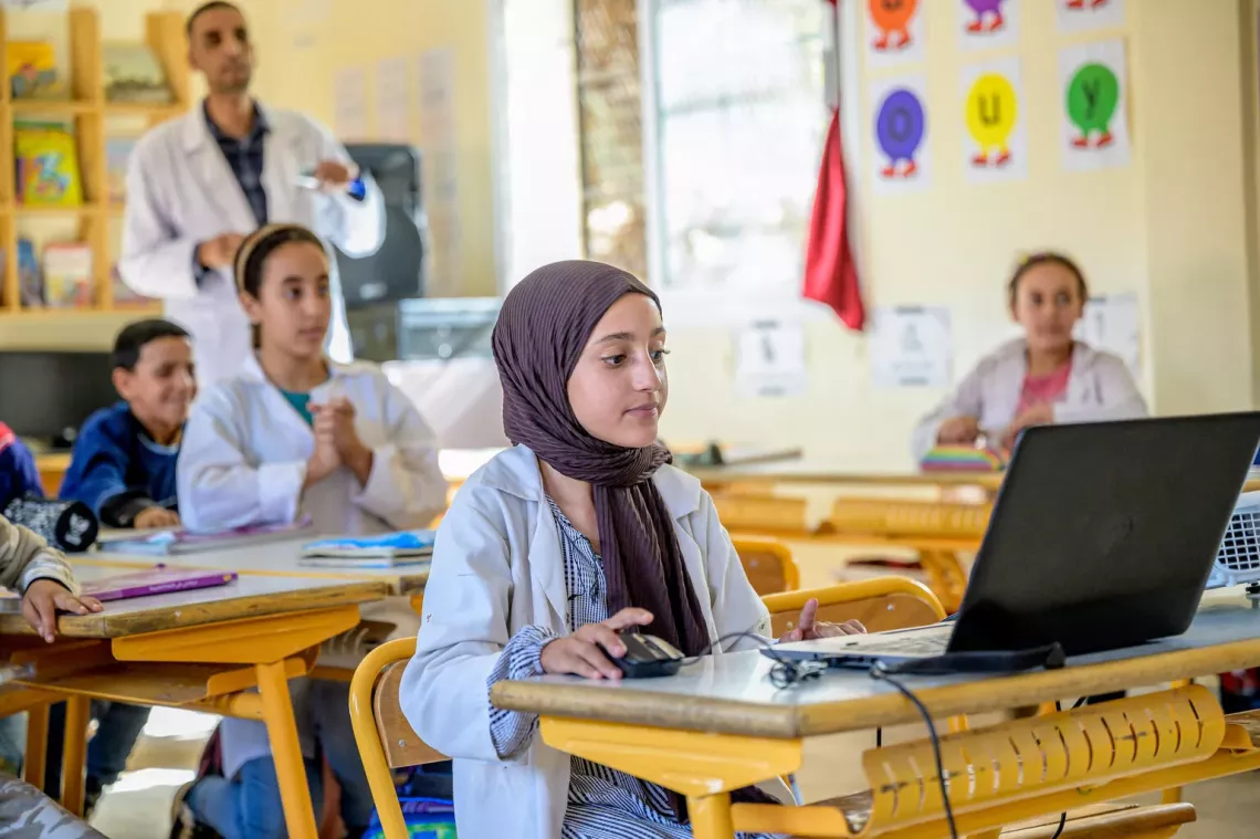 Une jeune fille marocaine, portant un uniforme scolaire, regarde attentivement l'&eacute;cran de son ordinateur dans une classe.