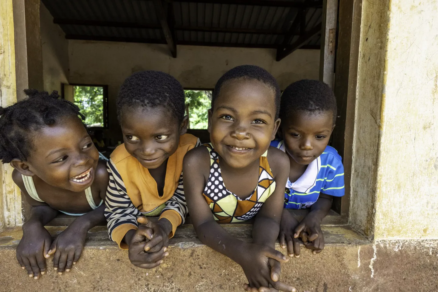 Um grupo de crian&ccedil;as em Mo&ccedil;ambique sorrindo apoiados numa janela de uma sala de auluas.