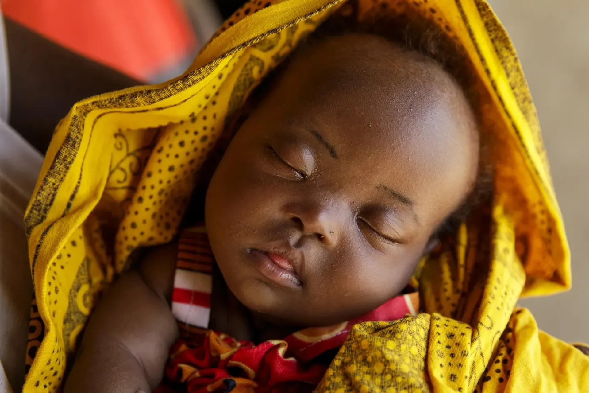 A baby sleeping wrapped in colorful blankets.