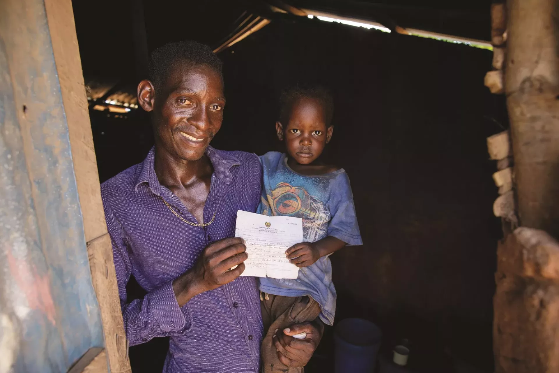 A man carrying his child in his arms shows his birth certificate from Mozambique.