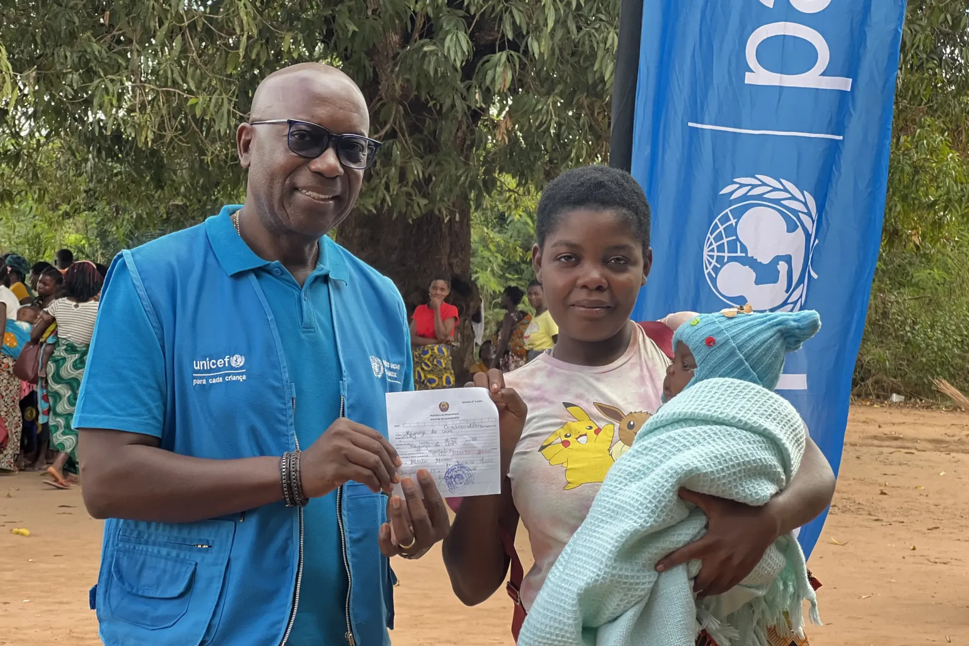 Michael Chimedza, UNICEF Mozambique Chief of field Office in Zambezia, holding a birth certificate with a young mother with a baby in her arms.