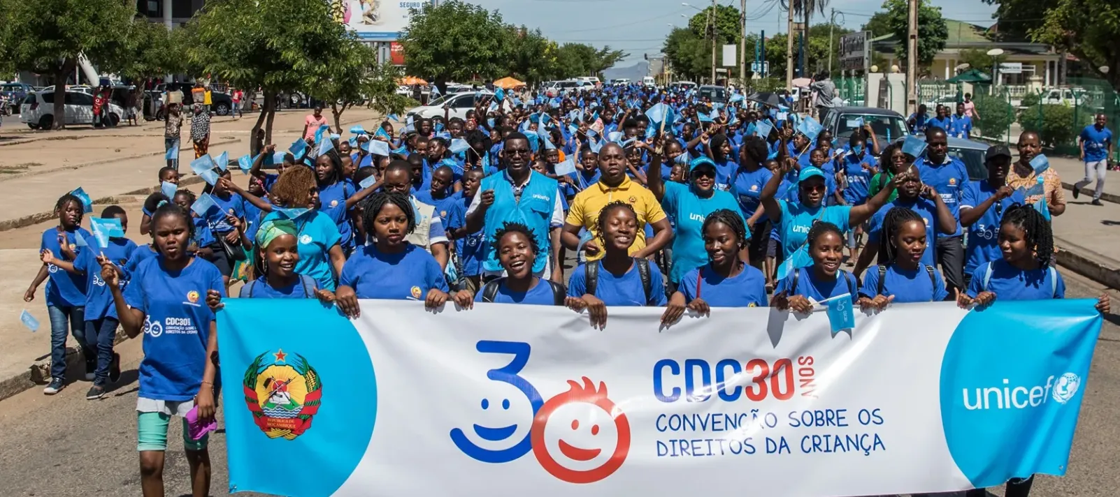 Large group of children and adults in blue shirts marching with a banner celebrating 30 years of the Convention on the Rights of the Child by UNICEF.
