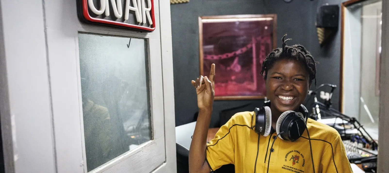 Girls smiling while pointing to a ON AIR sign inside a radio studio in Mozambique.