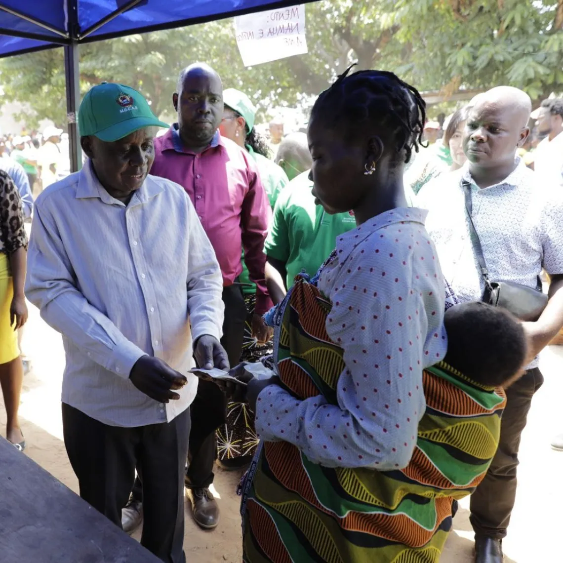 Vice Minister for Gender, Children and Social Action, Lucas Mangrasse, delivering money from child grant to a woman carrying her baby at the back, during the launch of Child Grant 0-2 years.