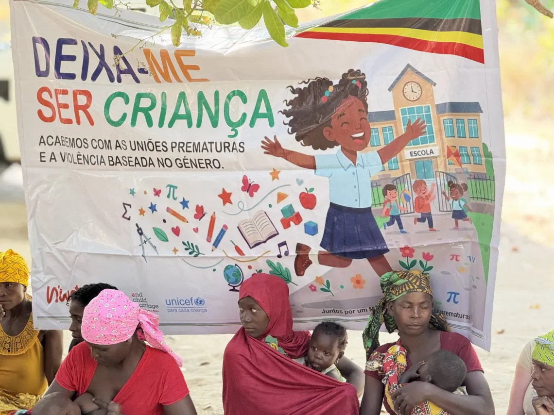 A banner reading "Deixa-me ser crian&ccedil;a" (Let me be a child) hangs above mothers and children at a UNICEF community dialogue in Nampula Province.