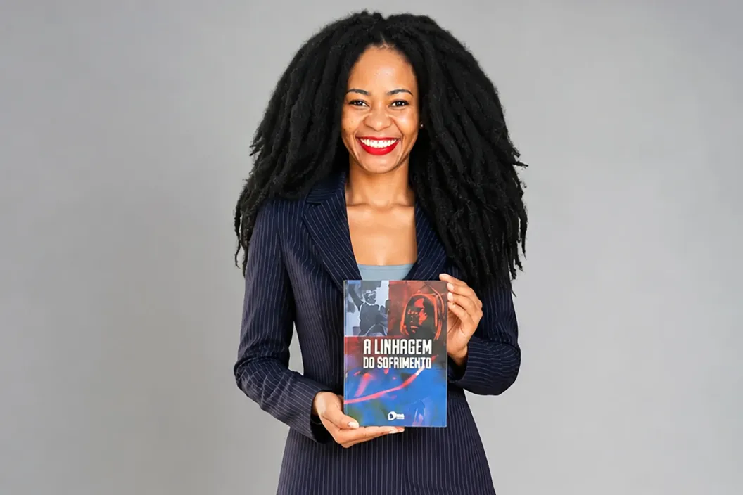 Mulher sorridente de blazer azul, cabelo crespo longo, segurando um livro colorido.