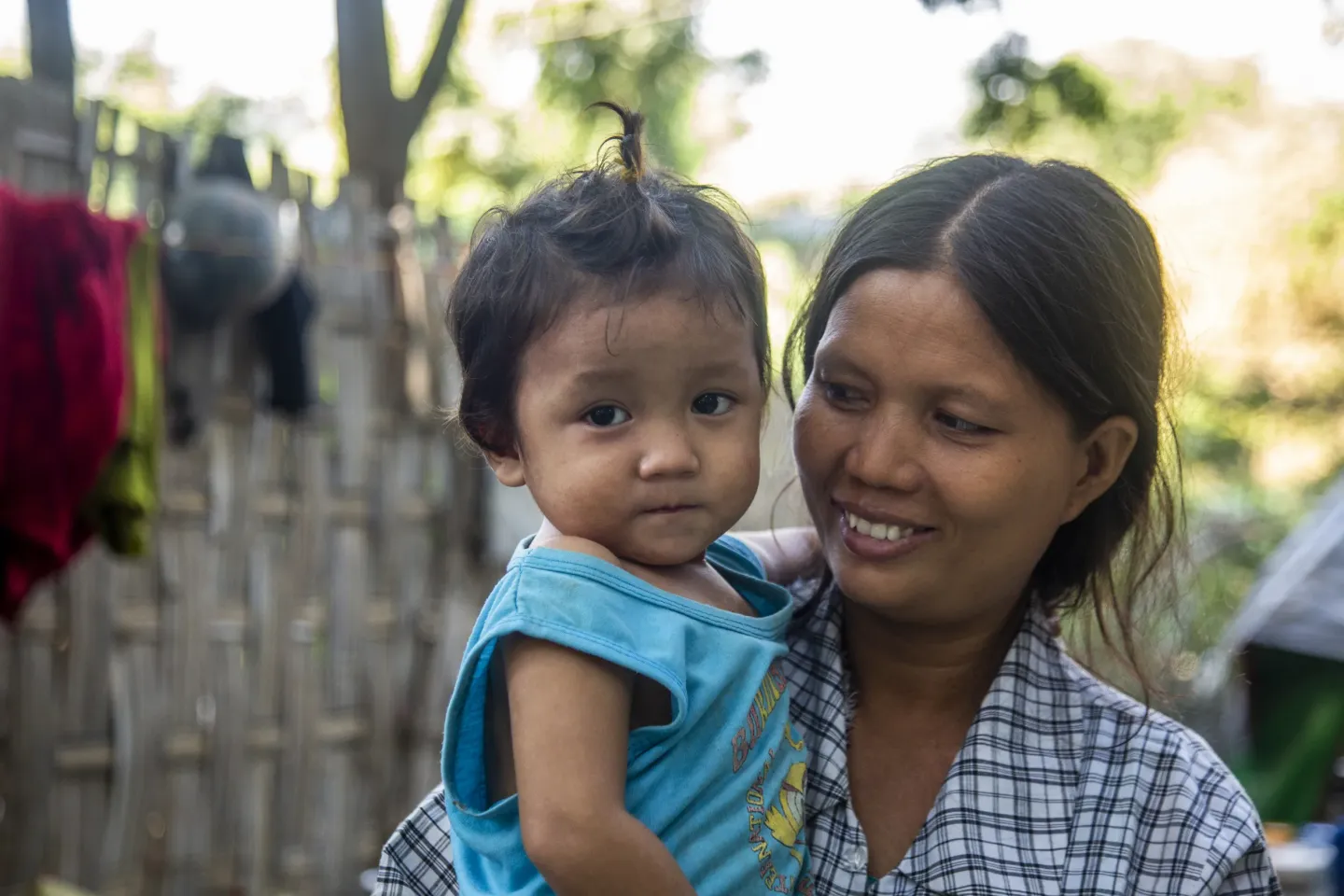 A mother holding her young child in front of their home. 