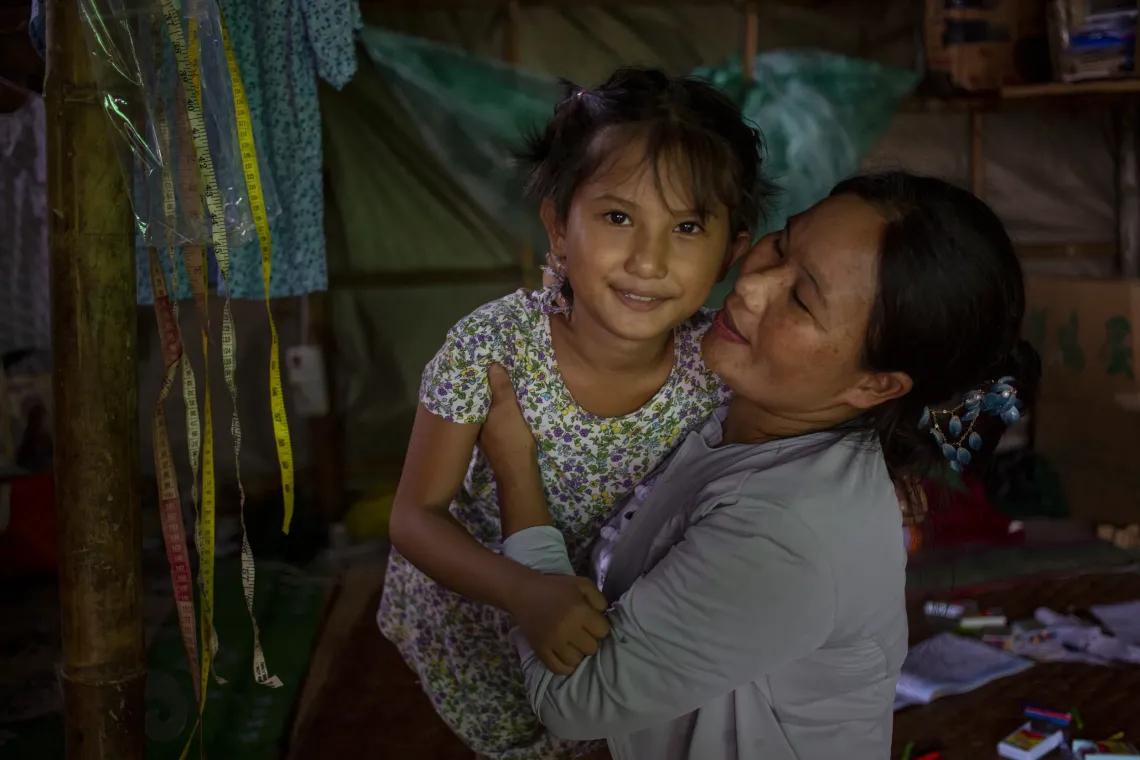 A mother hugging her daughter while the child looks into the camera. 