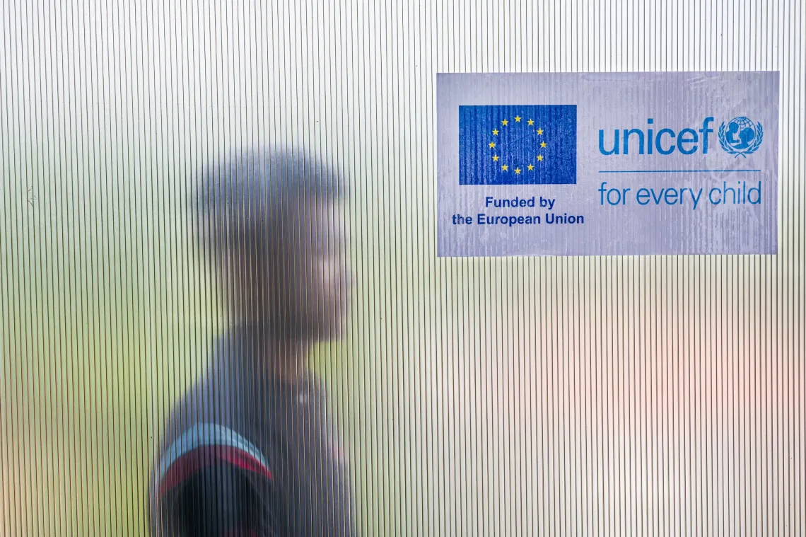 Photo of a young man behind a glass door. There is a logo of the European Union and UNICEF in the background. 