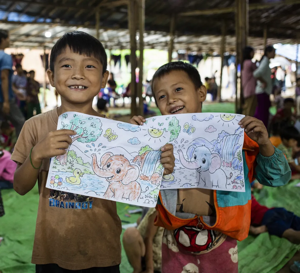 Two boys showing off their drawings during a child friendly space session inside a displacement camp. 