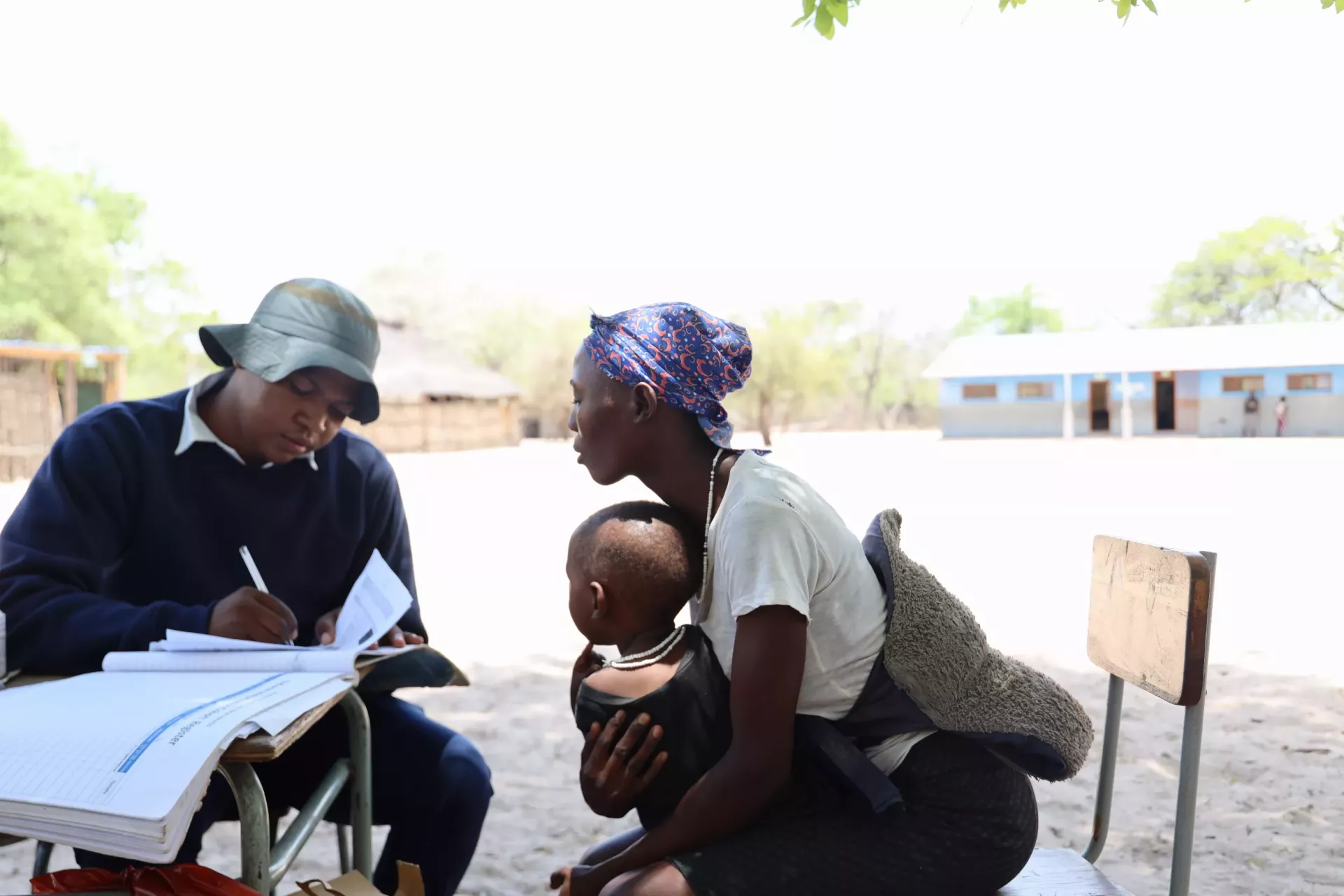 Nurse writing in a child's health passport while the mother sitting, with her baby on her lap, leans forward