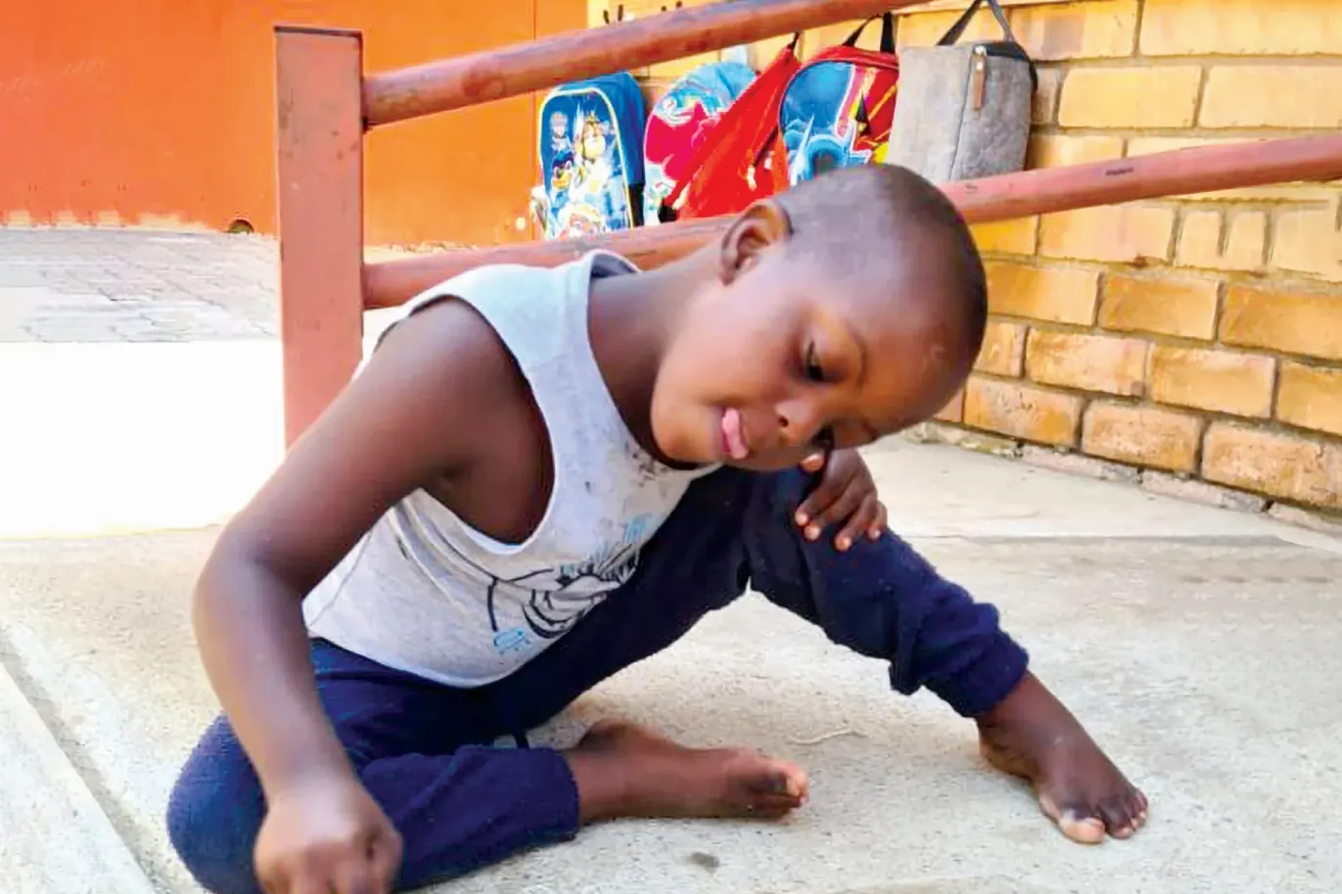 young boy at ECD centre sitting on the floor, writing with a piece of chalk
