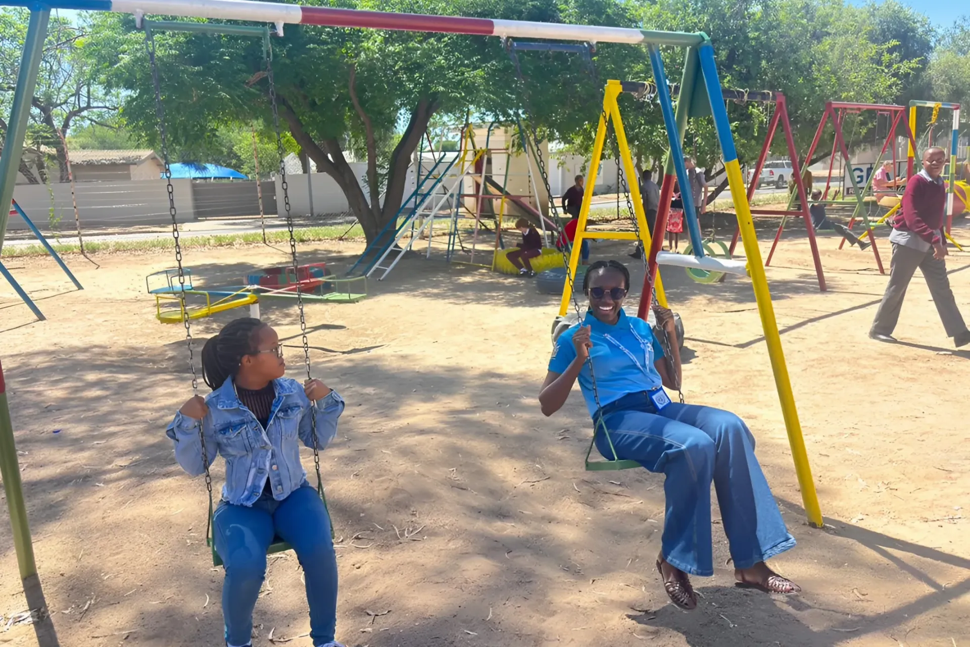 A UNV Girl swinging side by side with a young child on a playground 