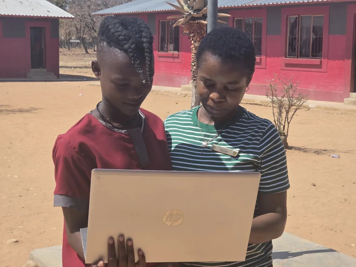 a teacher explains something to a young himba girl at school holding a laptop in her hands