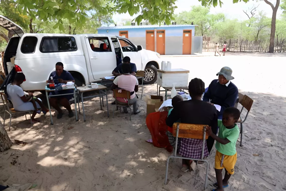 Nurse sitting behind a desk doing health screening of a child who is setting on her mother's lap