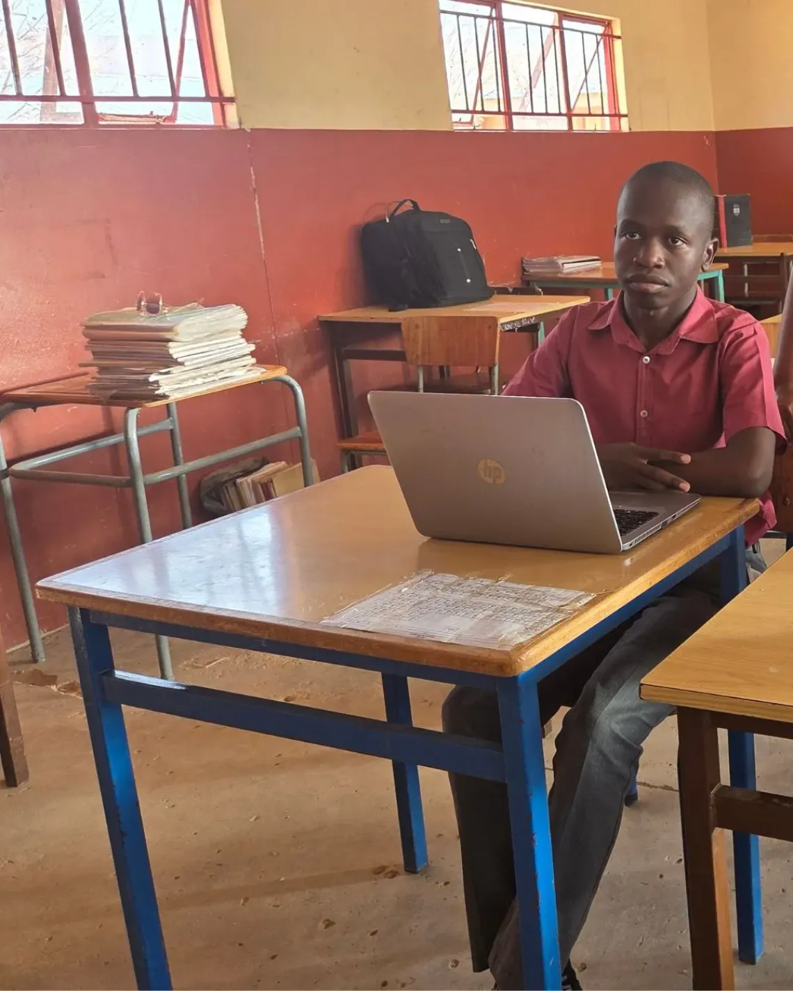 Boy learner sitting in a classroom, behind his desk, with a laptop in front of him.