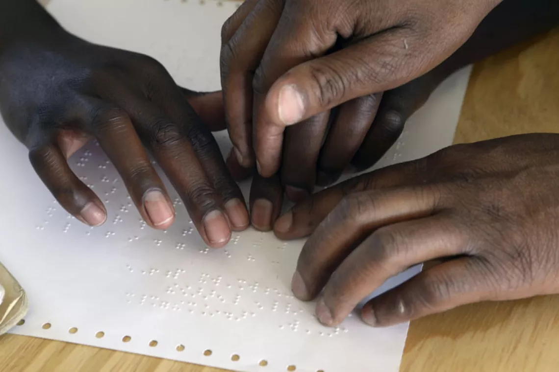 Teacher showing girl child with visual impairment how to read braille