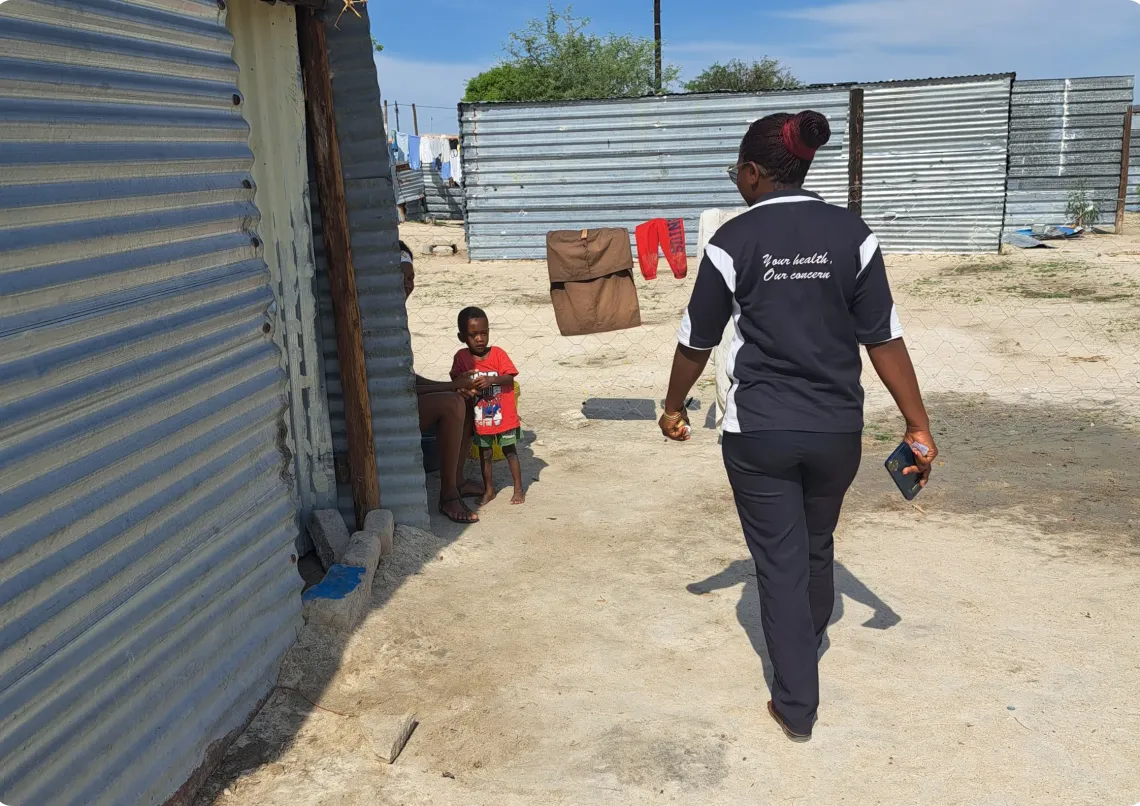 A community health worker visits a house with a little boy watching her approaching him
