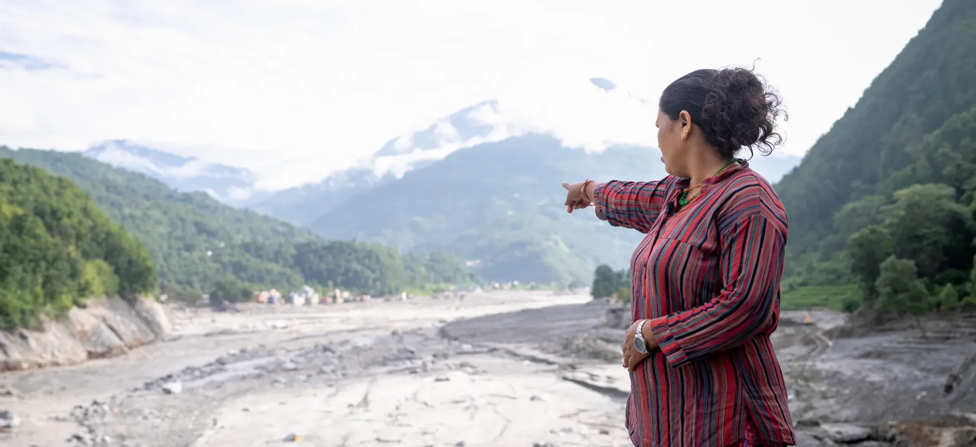 Shobha Adhikari points toward the wide, grey stretch of stones and silt below.