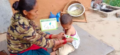 This image shows A mother in Kalikot District measures arm of her child using a MUAC tape after receiving a short orientation on family MUAC