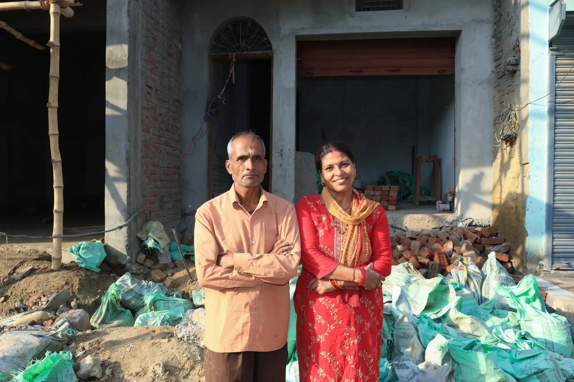 Group photo of Lila (wife) and Uttam (Husband) in front of their house. 
