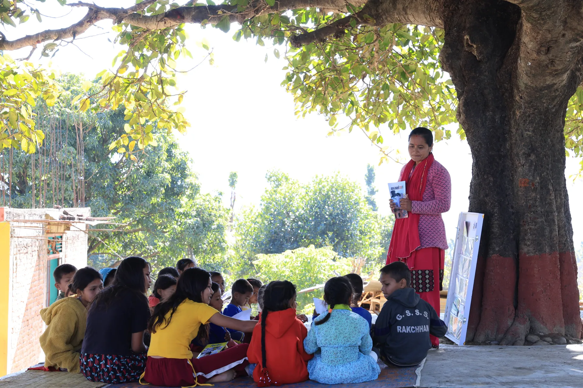 A view of a teacher outdoors with children under a tree