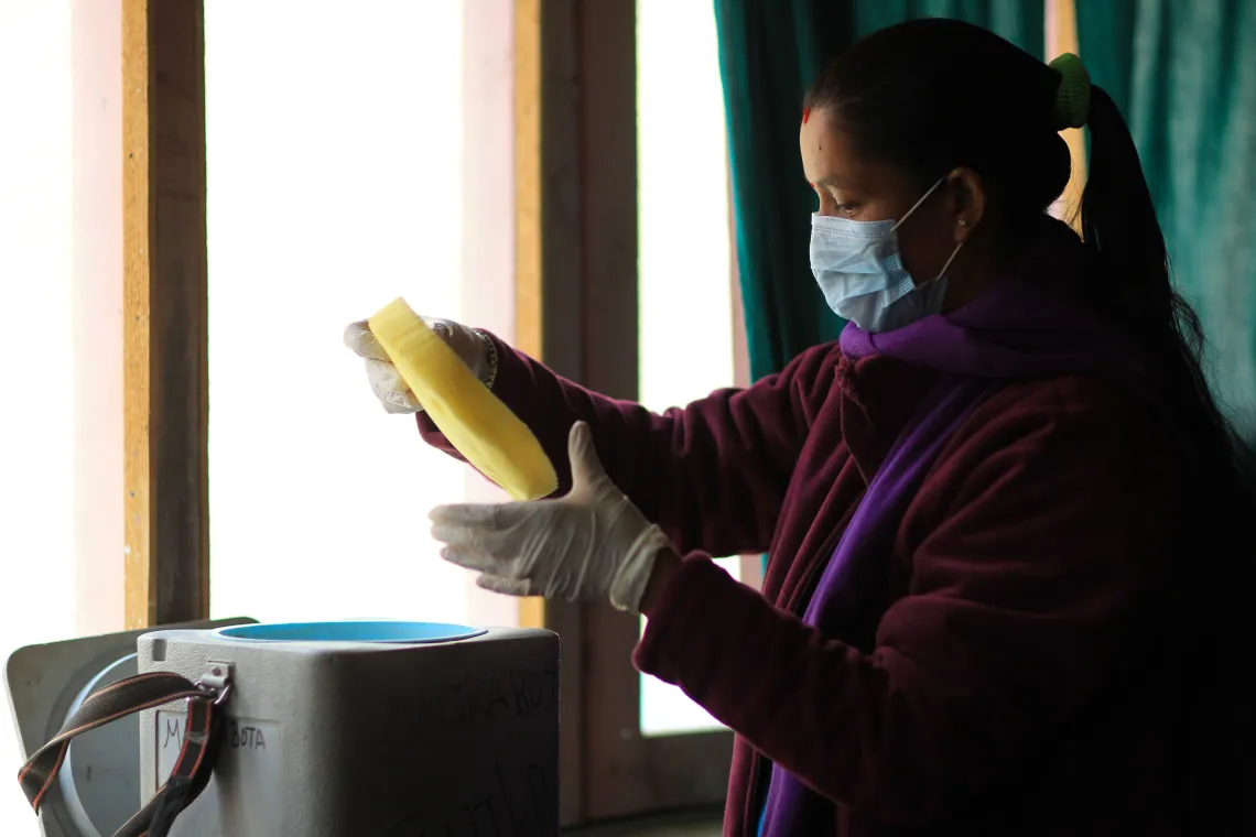 This image shows auxiliary nurse midwife Ganga Devkota unpacking COVID-19 vaccines at the Malikabota Health Post