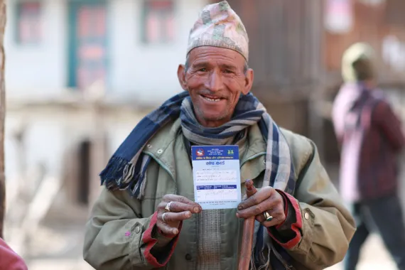 This image shows an elderly man from Jumla holding up his vaccination card