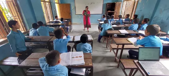 A classroom filled with students are listening to the female teacher.
