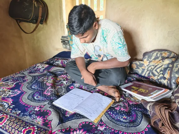 Mahendra sitting on his bed reading ALP materials