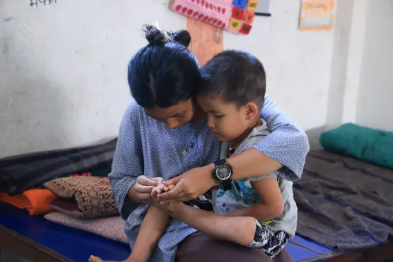 On 27 August 2026, Sonika (13) holds her younger brother Sajan (3) in a school in Nuwakot District where the family have been staying since escaping the floods that destroyed their home and village on 26 August. When the floods hit Bhaise, Sonika ran uphill carrying her brother. Behind her, the family home where generations had lived was swept away.