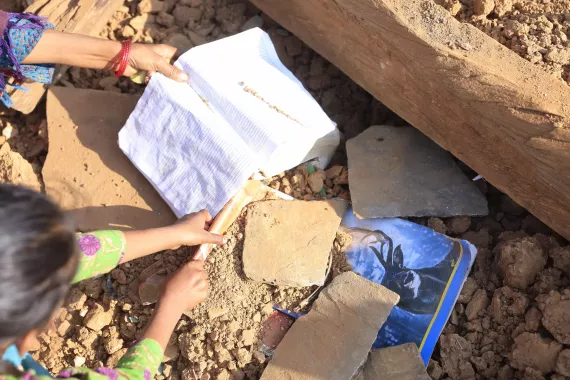  8-year-old Srijana BC digs through rubble to find her books.