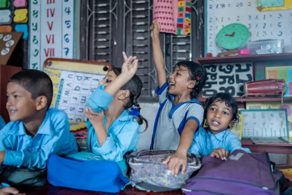 A group photo where young students are raising their hands with a smile on their face  
