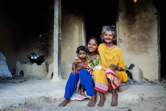Laxmi, her grandmother and her sibling sitting in front of their house 
