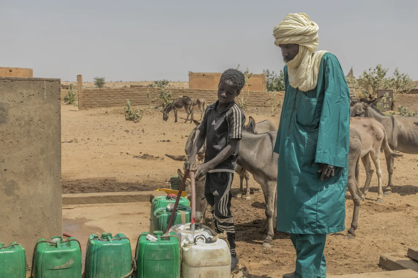 A man is watchin a boy filling jerry cans at the fountain. 