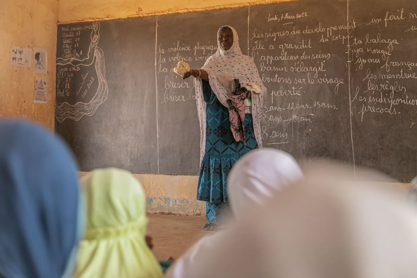 Ramatou Hassan holds a sponge in front of the blackboard, demonstrating what is in the menstrual hygiene kit to the school class.