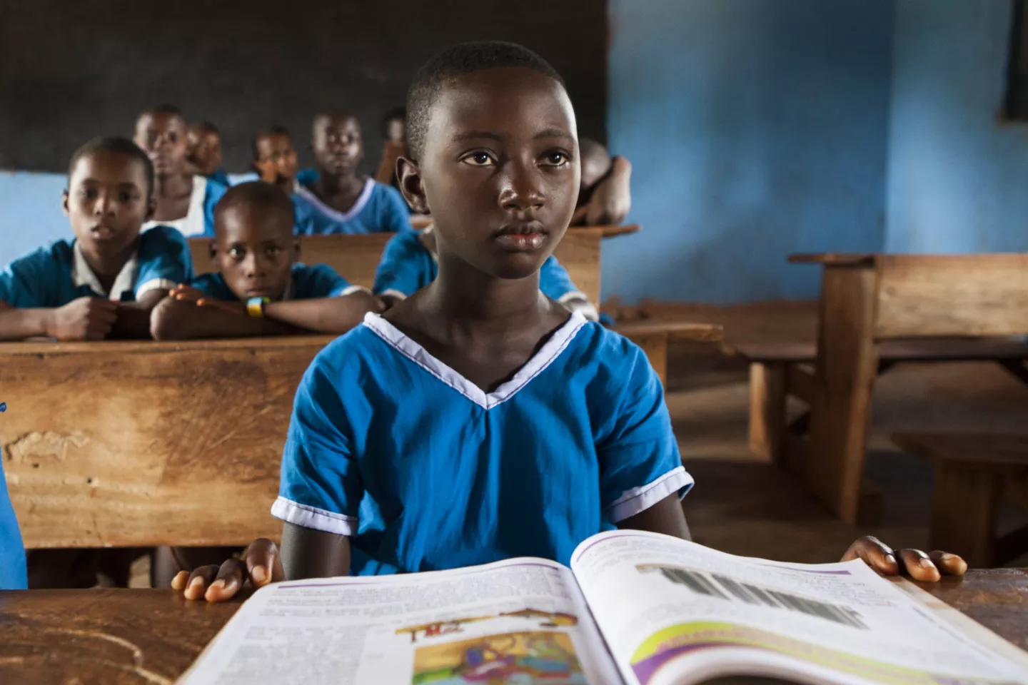 A schoolgirl in a classroom with an opened book in front of her.